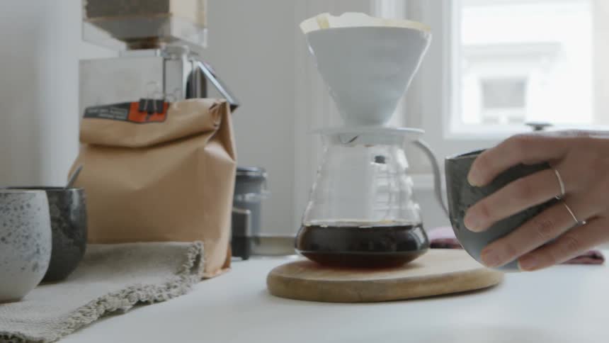 Woman selects ceramic mug then checks dripping coffee