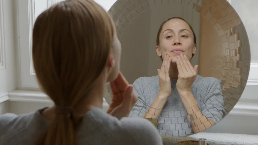 A woman puts a cream on her face and rubs it into her skin