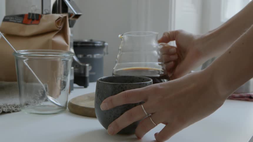 Woman pours coffee from a glass decanter into a mug