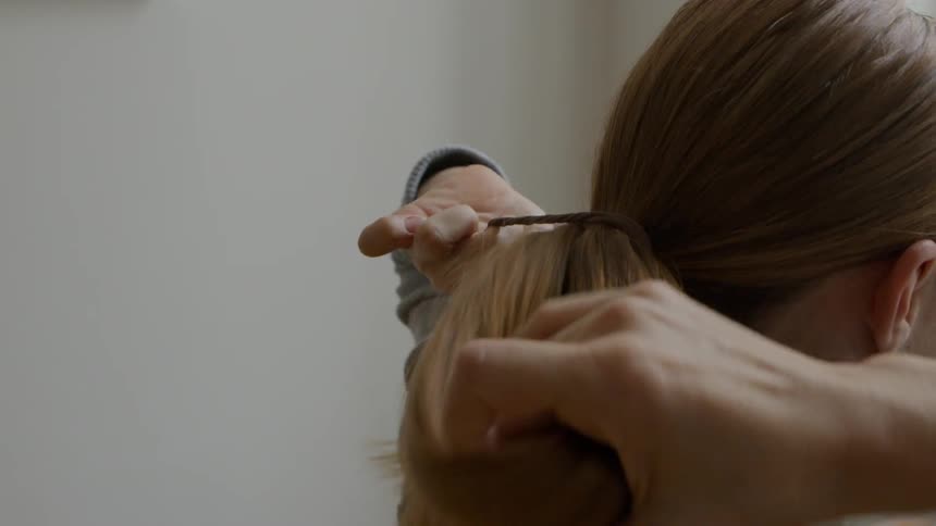 A woman puts her long hair into a ponytail with a black elastic