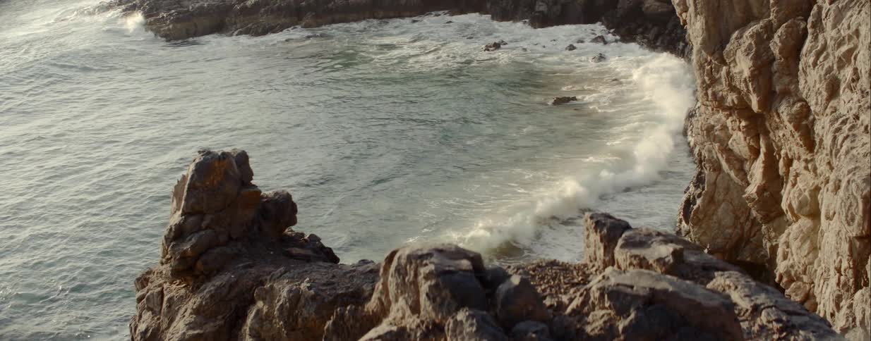 Ocean waves curl and splash against the rocks and cliffs on shore