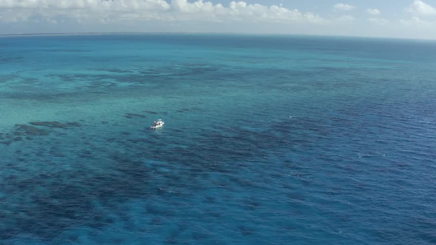 Wide shot of boat in vast bright blue ocean in daytime