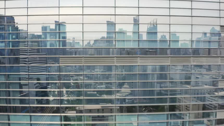 Skyscrapers are reflected in a tall glass building in a city