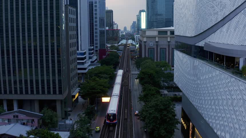 Vehicles drive alongside a passenger train passing through a dense city