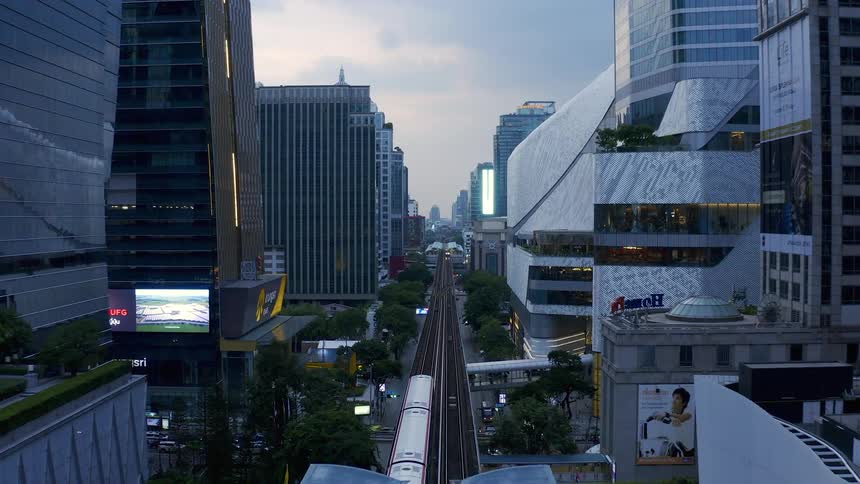 A passenger train passes by traffic and tall buildings in a modern city