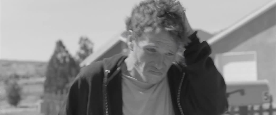 A man walks down the street rubbing his head