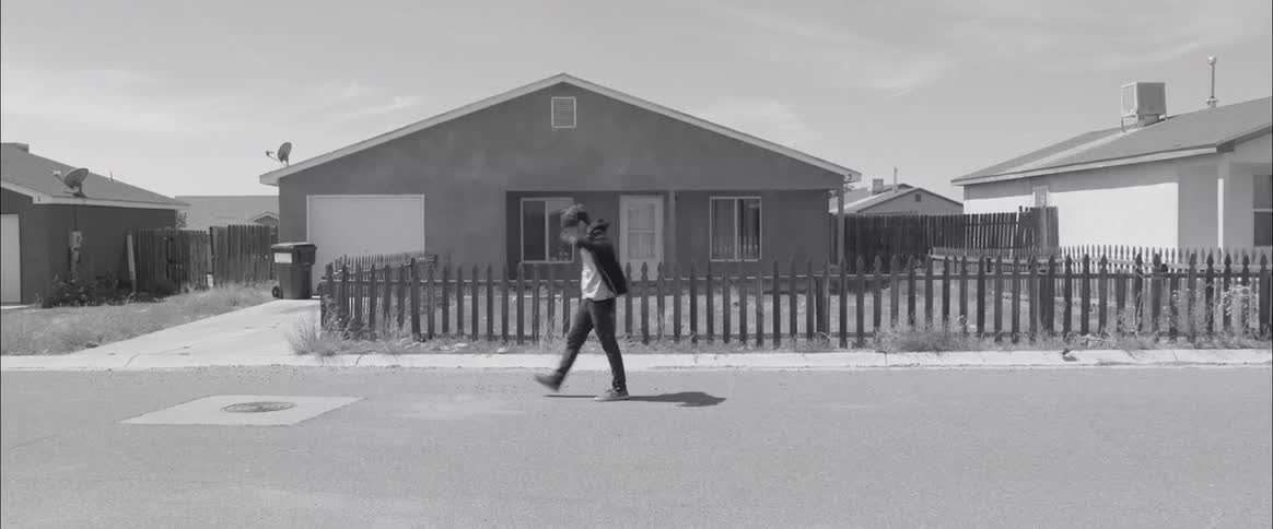 Man gestures wildly as he back and forth in street in front of houses