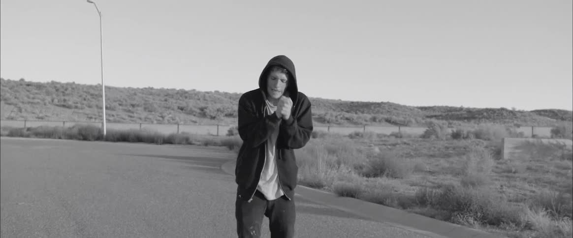 An angry man in a hoodie grasps his hands together outside