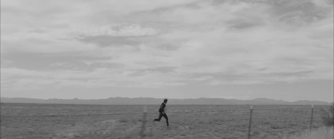 A man runs alongside a barb wire fence in a field