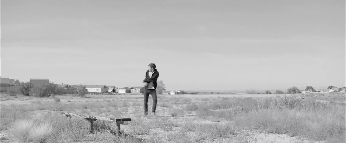 A man walking through an open field appears to be bothered by some small and unseen bugs