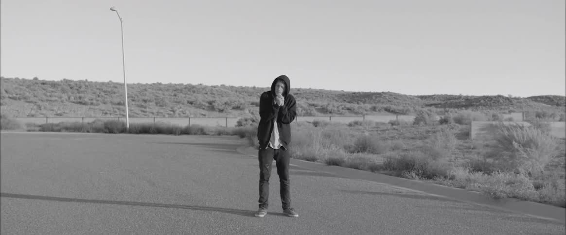 Black and white footage of man wearing hoodie standing outdoors praying
