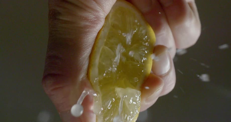 Person squeezes sliced lemon half splashing juice around