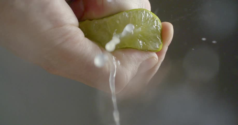 A man squeezes a lime that is cut in half while the juice squirts