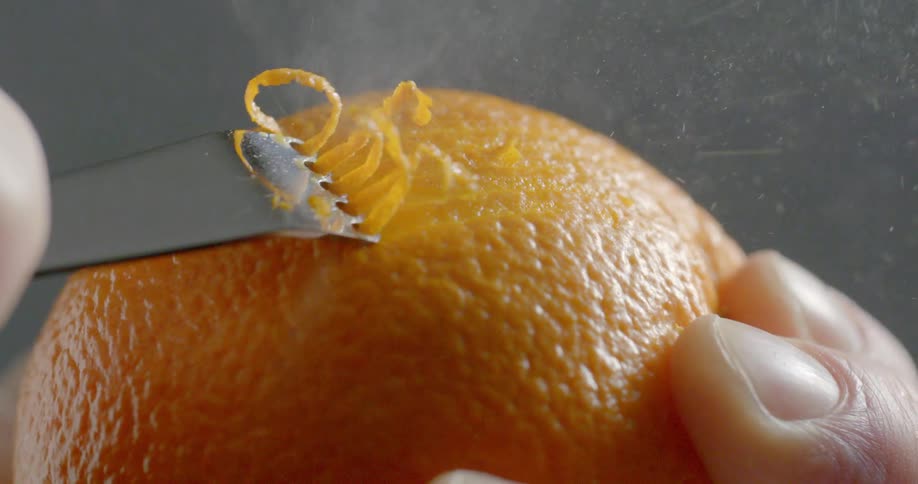 A tool crosses along the outside of an orange to peel the zest