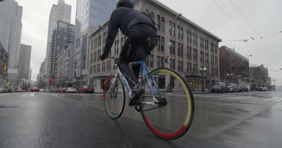 A man is riding his bike down a city street on a cloudy day