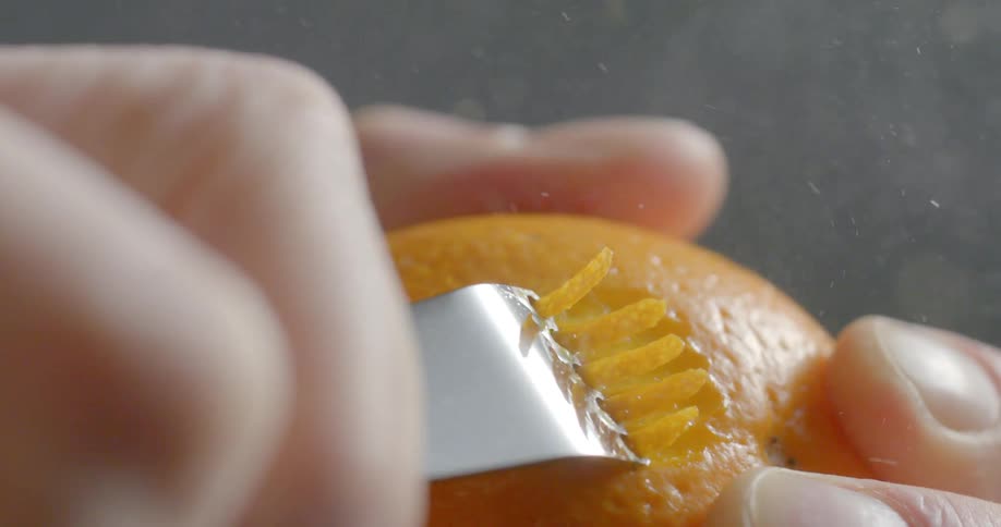 A woman uses a zester on an orange
