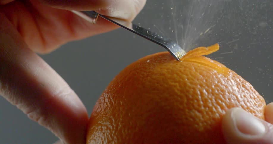 A tool runs against the skin of an orange to create zest