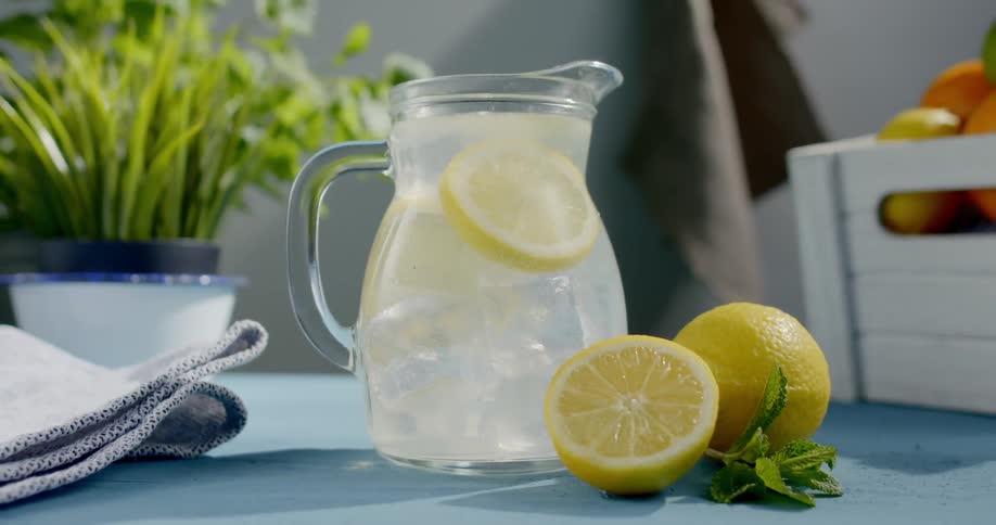 Person places pitcher of water near sliced lemons on table