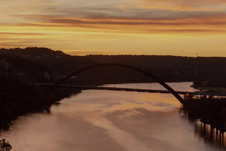 Cars drive over a bridge as clouds float in the sky at sunrise
