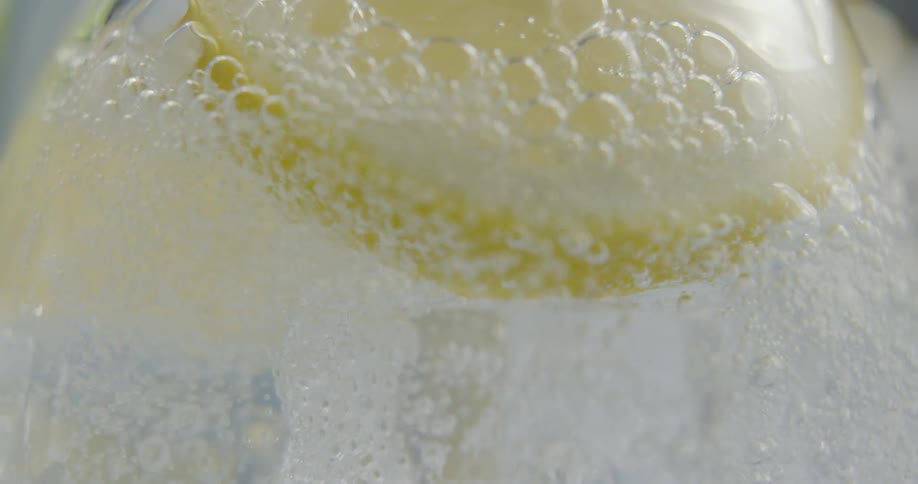 Carbonation bubbles float around a lemon slice as a beverage is poured into a glass
