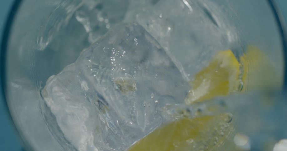 Water pouring into tall glass filled with ice and lemon slice
