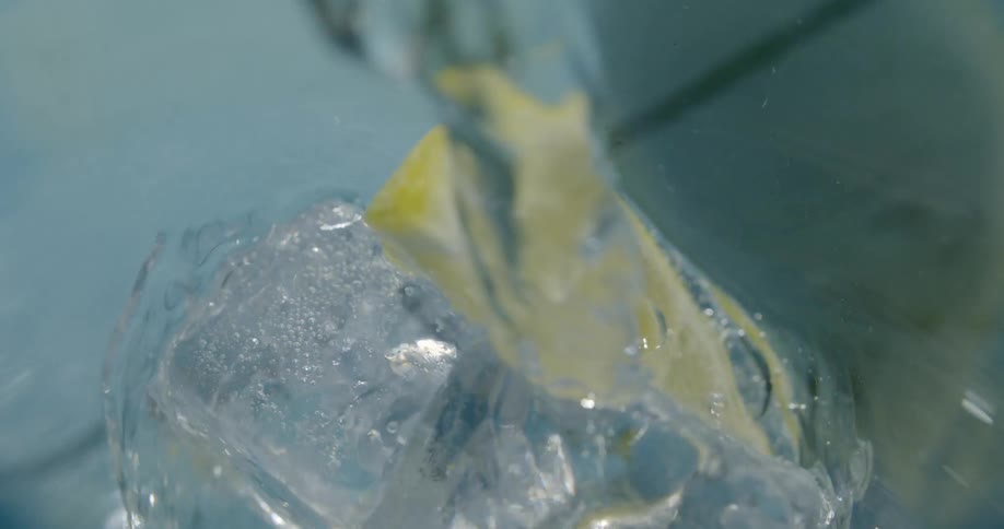 Water is poured into glass over ice and a lemon wedge