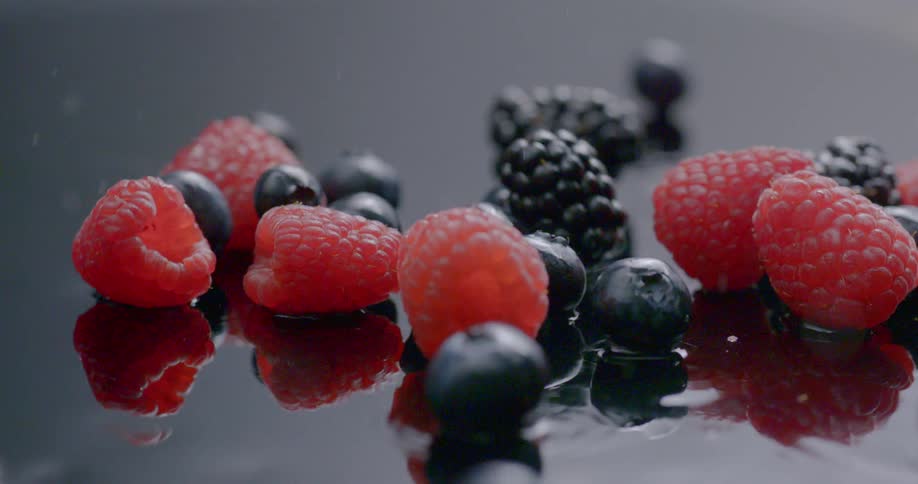 Raspberries blueberries and blackberries fall onto a watered surface