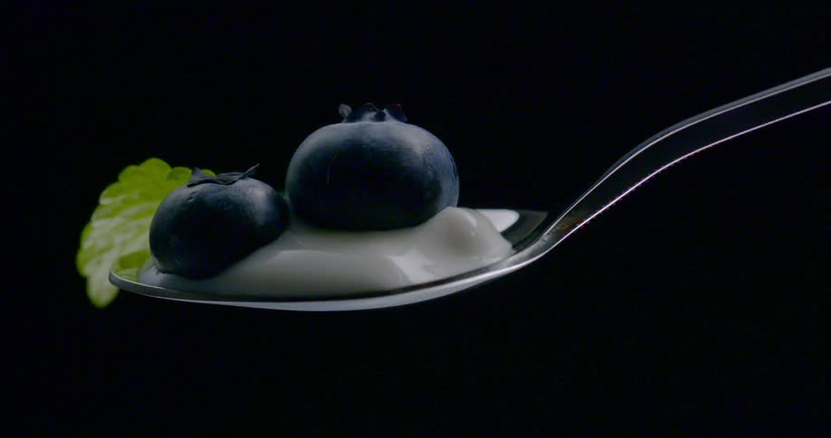 Blueberries and cream rest on a spoon with a mint leaf