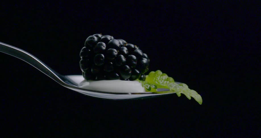 A blackberry rests on yogurt on a spoon