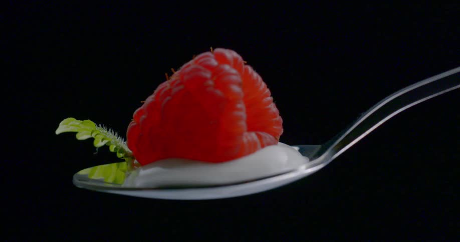 Raspberry sits on a bed of cream on a silver spoon