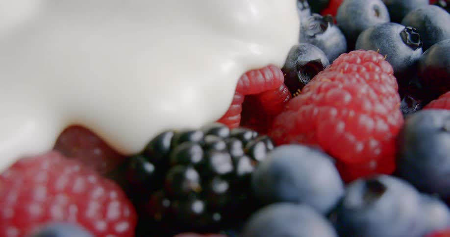 Cream is poured slowly as it covers a mixture of fresh red raspberries blue berries and black raspberries