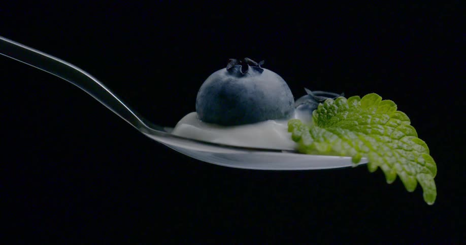 A blueberry sits in yogurt on a spoon