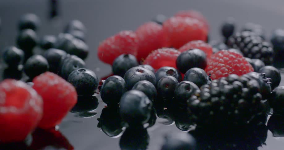 Raspberries blackberries and blueberries are dropped on to a wet surface