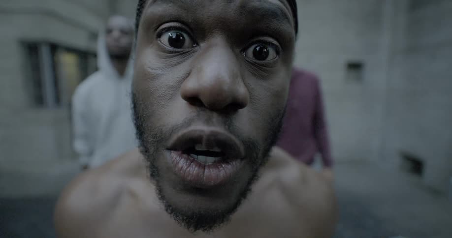A black man yells at someone as two other men stand behind him