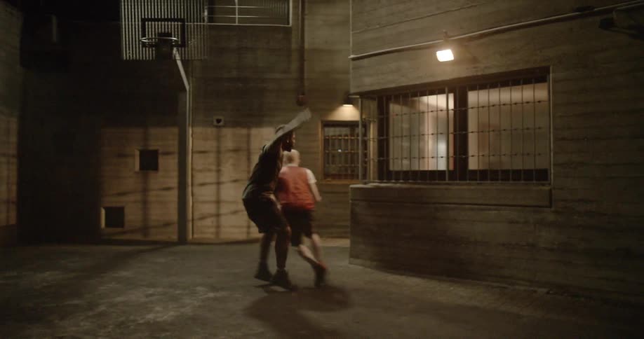 A group of young men play basketball outside at night
