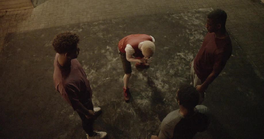 Three men watching as an albino man climbs to his feet with a basketball