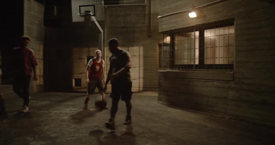 Men play basketball at night causing one to fall