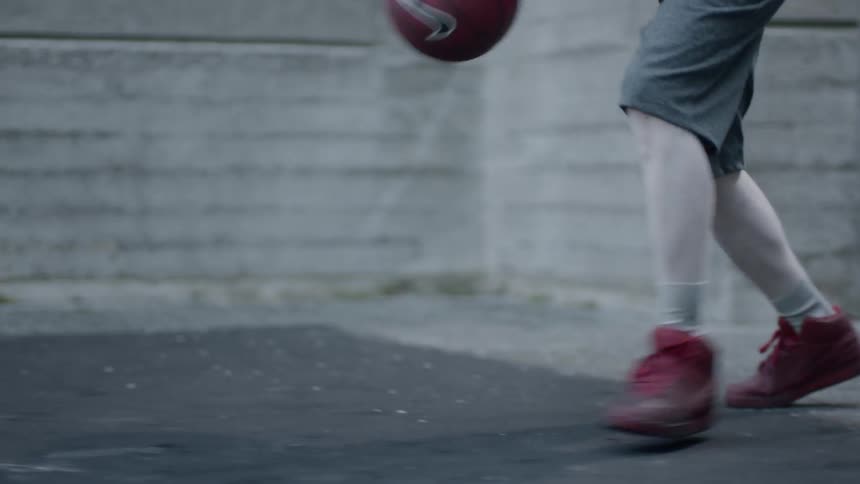 A male wearing red sneakers and shorts dribbles a basketball in an enclosed brick courtyard
