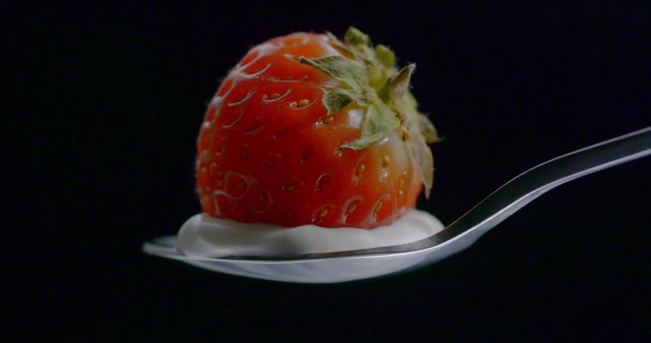 A spoon holding yogurt and a strawberry