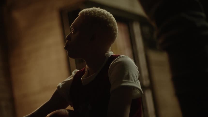 A teenage basketball player sits on the floor and gets up