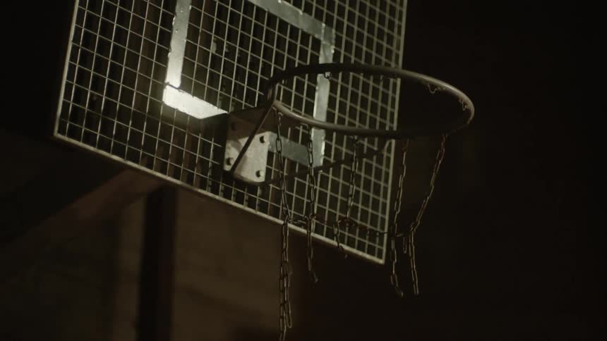 A basketball hoop with chains shakes at night