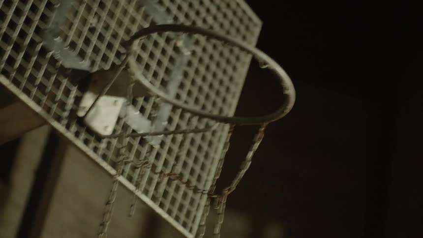 A basketball hoop with a grid backboard and a broken chain for a net