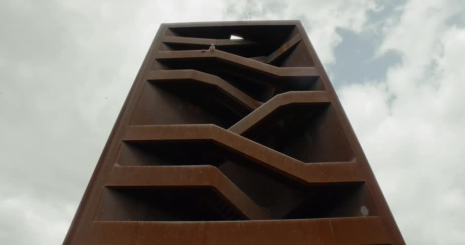 A basketball is dropped from a tall tower as clouds float overhead