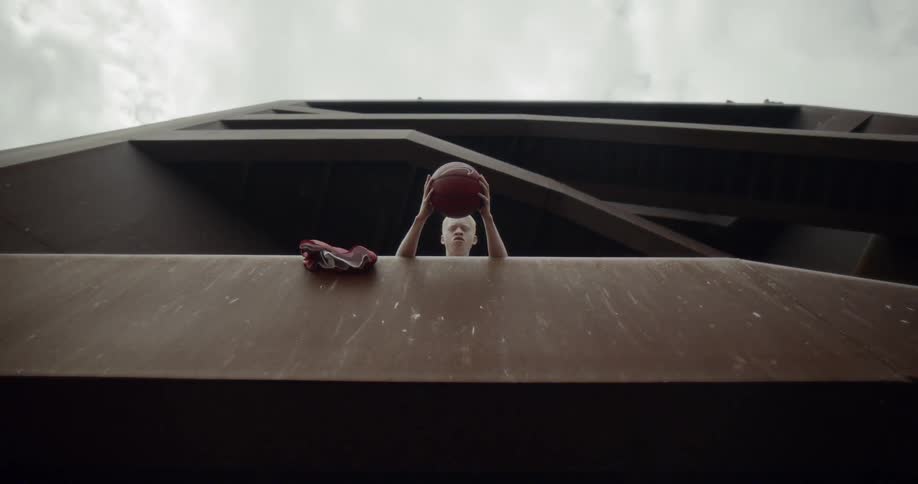 A man leans over the edge of a balcony with a basketball in his hands