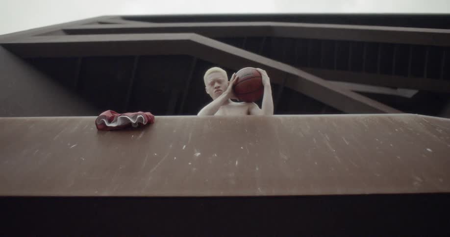 A young man is looking down from a level of outdoor stairs while holding a basketball