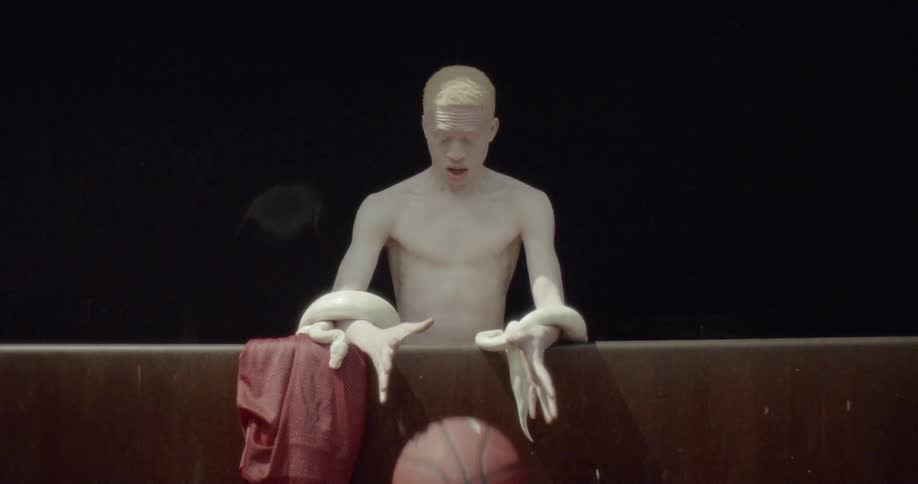 Pale man with white constrictor wrapped around him drops basketball