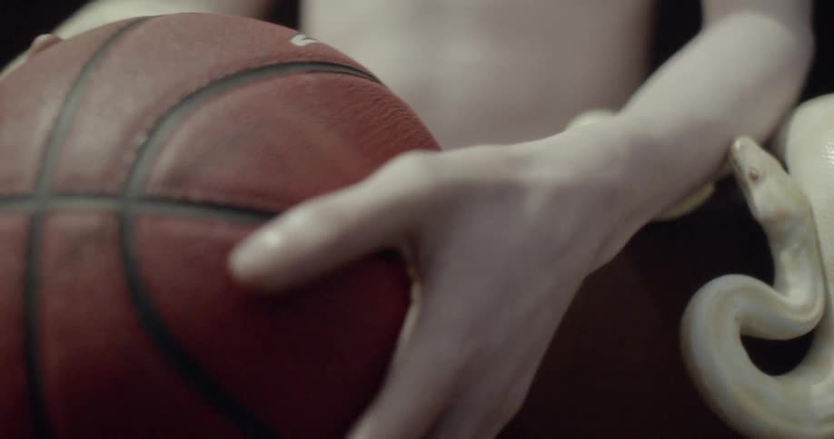 A teenager drops a basketball as an albino snakes sits around his arms