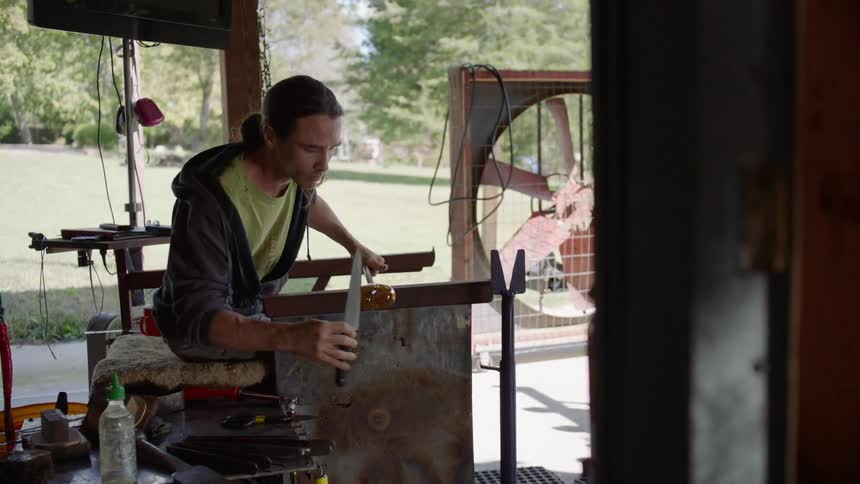 A man is using a knife to form glass on a stick