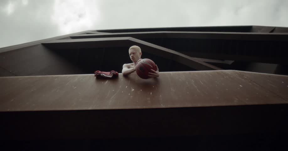Albino man holds basketball from a balcony on a building