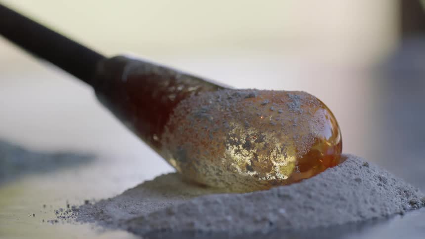 The translucent bulbous end of a rod being rolled in a powder